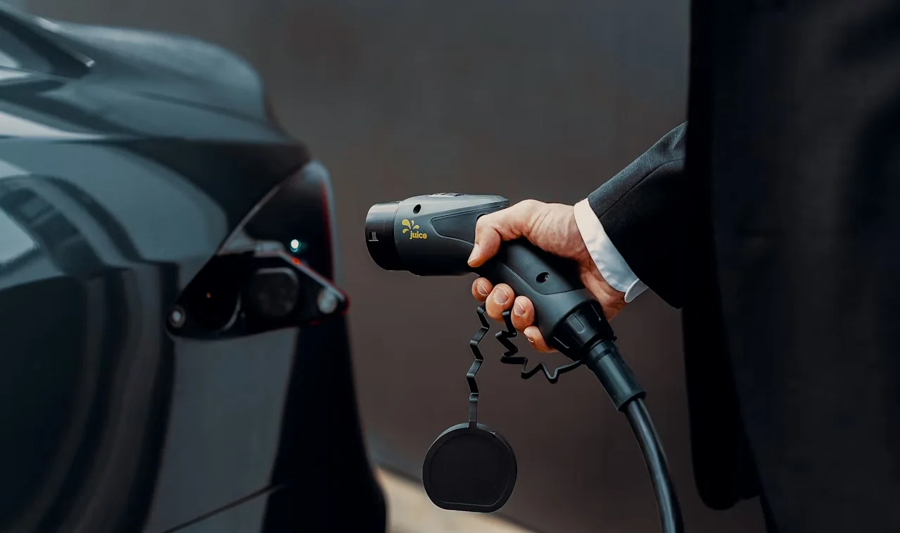Hand holding an EV charging connector beside a car